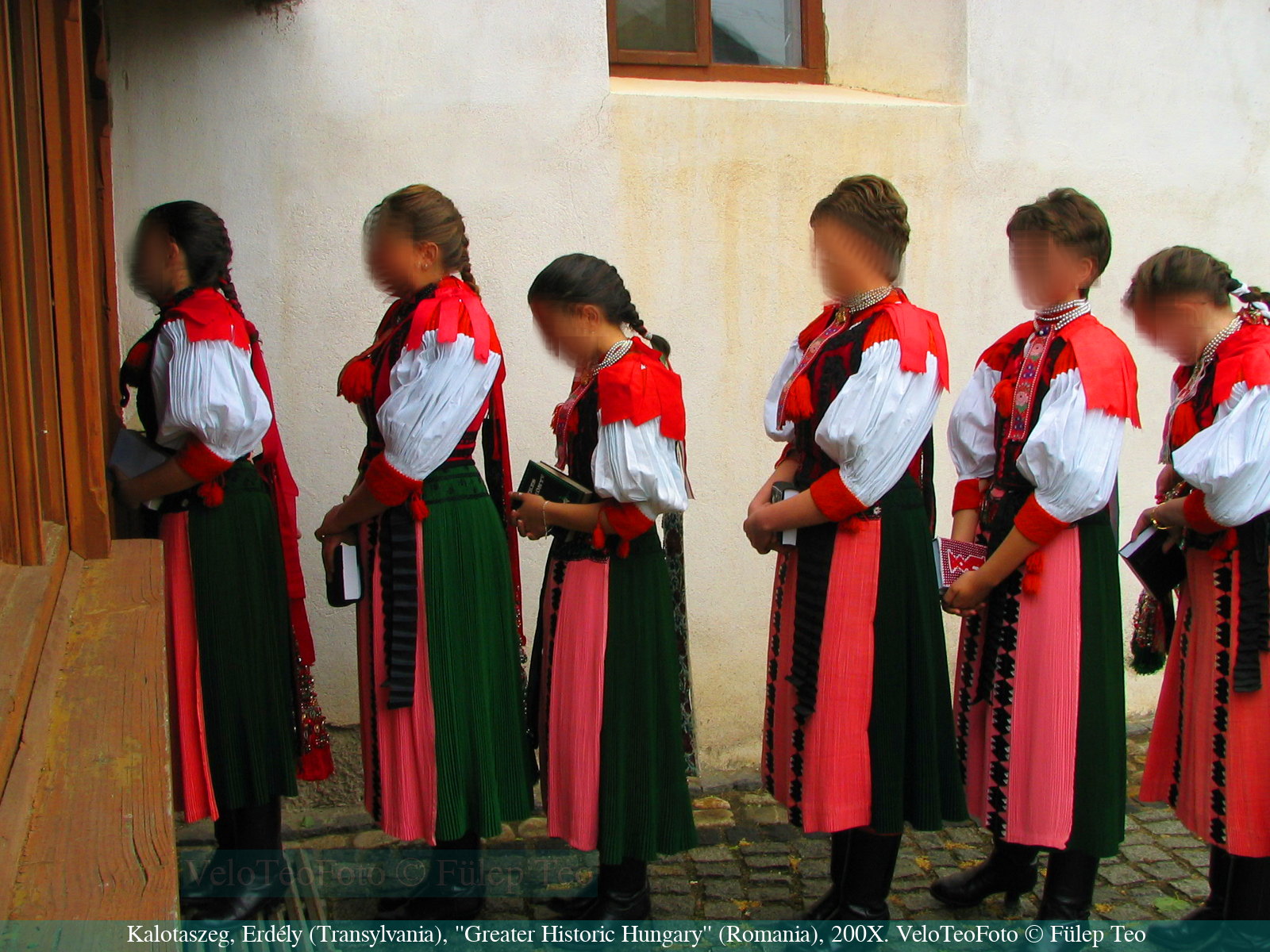 Kalotaszegi népviseletbe öltözött lányok sorakoznak konfirmálásra egy református templom kapujánál, valahol Kalotaszegen, a kétezres évek elején. A népviselet itt még az élet része, míg nálunk már múzeum és színpad.